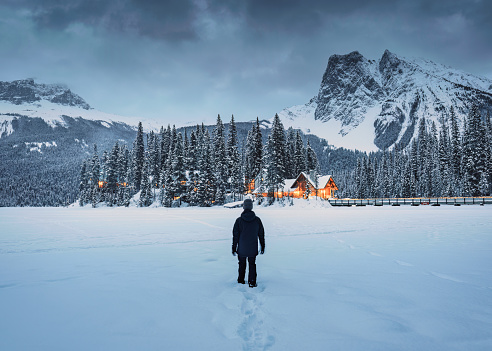 A traveler man standing in snowfield with wooden lodge glowing and pine forest in rocky mountains at Yoho national park, Alberta, Canada