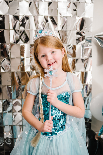The girl is dressed in a blue dress of Elsa. Happy child celebrating a birthday party. Photo wall decoration white, black, and silver balloons. Idea decor an arch in luxury style. Closeup princess.