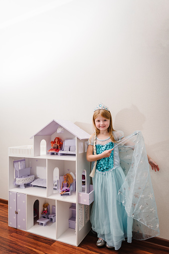 The girl is dressed in a blue dress of Elsa. Happy child celebrating a birthday party. A happy and surprised little girl is playing with a doll house. Closeup princess.