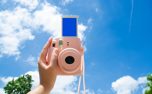 Hands Holding and shooting an empty screen photo frame Instant Camera with blue sky view on background.
