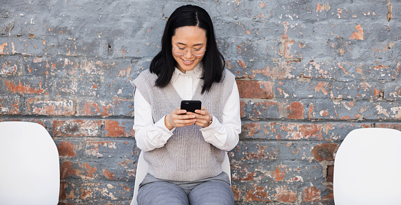 Woman texting, waiting for interview on chair and typing on phone, recruitment and employment with smile. Happy person in Japan sitting on chair, smiling and excited for job opportunity for people.