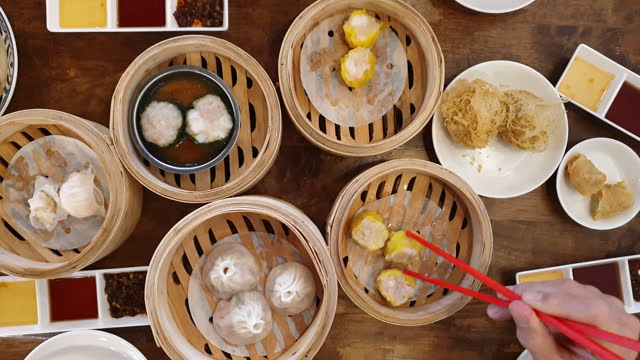 Hands chopsticks eating dim sum shu mai Chinese hong kong style breakfast food steamed dumplings stuffed bao