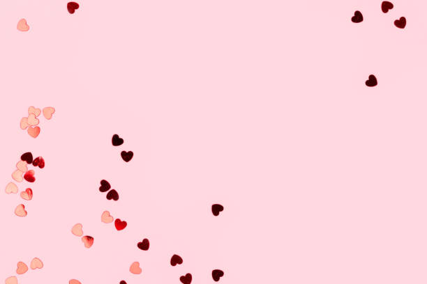 istock Metallic red confetti in a heart shape scattered on a pink background. 1474835032