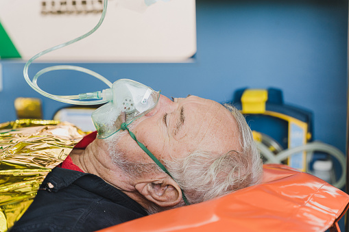 close-up of a elder man in a ambulance wearing oxygen mask and lying on a stretcher unconscious