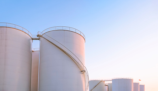 Group of storage fuel tanks in oil industrial manufacturing area against clear sky background in evening time, low angle and perspective side view