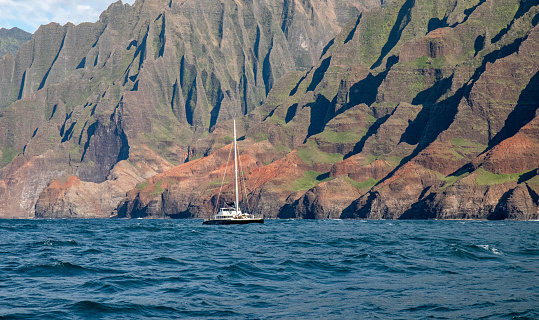 A sailboat dots the Pacific Ocean on the Napali Coast of Kauai