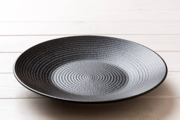 istock Perspective view of empty black plate on wooden background. Empty space for your design 1474845989