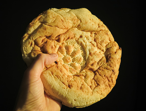 A fresh flatbread in a man's hand in close-up on a dark background with selective focus. A flatbread in a man's hand close-up. Traditional bread.