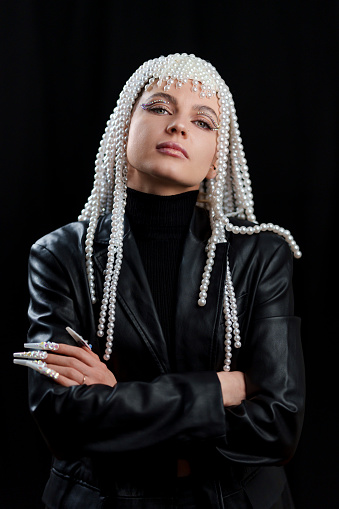 Vertical studio portrait of a cool woman with fake nails and a wig of pearls looking at the camera