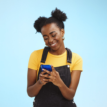 Black woman with smartphone in hands, smile and happy with chat or social media, communication isolated on blue background. Technology, happiness and gen z youth, phone with internet wifi and mockup