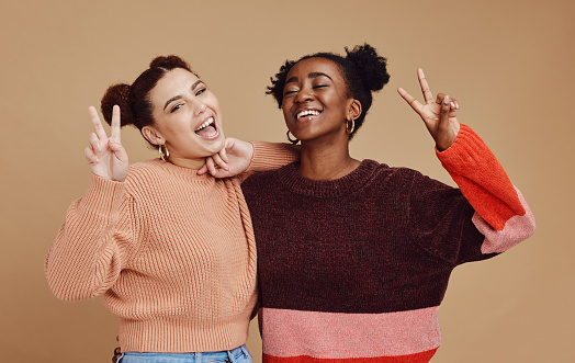 Fashion, peace sign and women friends in studio with hand gesture, smile and happiness on brown background. Freedom, beauty and black woman with happy girl for relaxing, cosmetics and emoji together