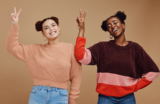 Beauty, peace sign and women friends in studio with hand gesture, smile and happiness on brown background. Fashion, cosmetics and black woman with happy girl for relaxing, chill and freedom together