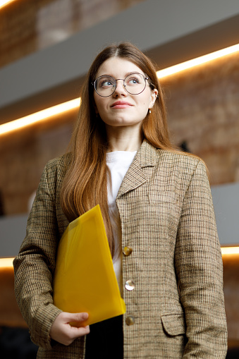 A young woman in a jacket with a yellow folder on the background of the office, purposefulness.