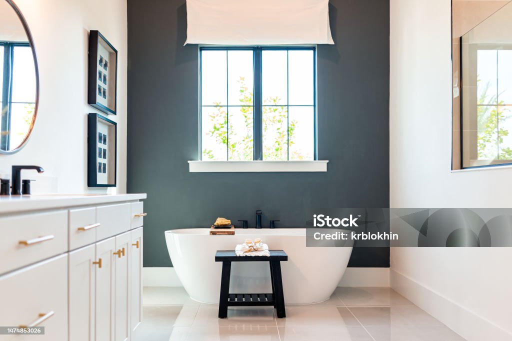 Bathtub in bathroom staging model home house or hotel with modern luxury white cabinets interior, window with light and mirrors Bathroom Stock Photo