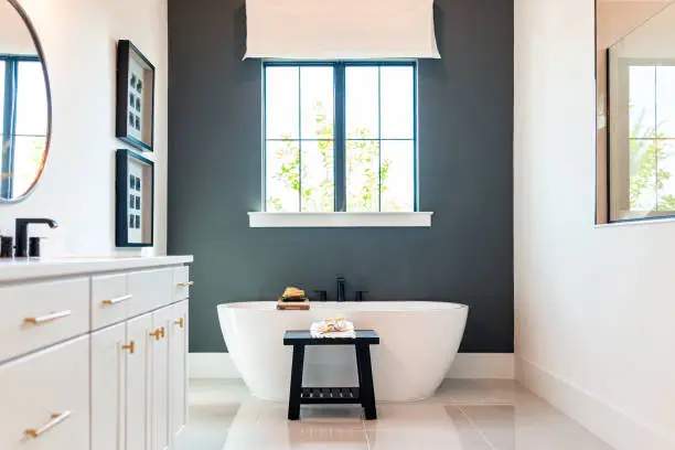 Bathtub in bathroom staging model home house or hotel with modern luxury white cabinets interior, window with light and mirrors