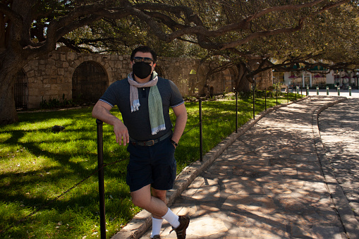 Caucasian Mexican man visitor wearing mask and sunglasses to avoid contagion covid 19 on Alamo sightseeing in San Antonio Texas on street next to the garden