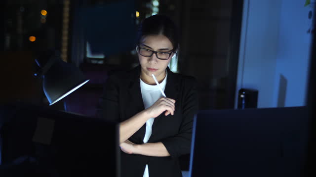 Asian woman using computer to video call for business meeting while working late at night at home office