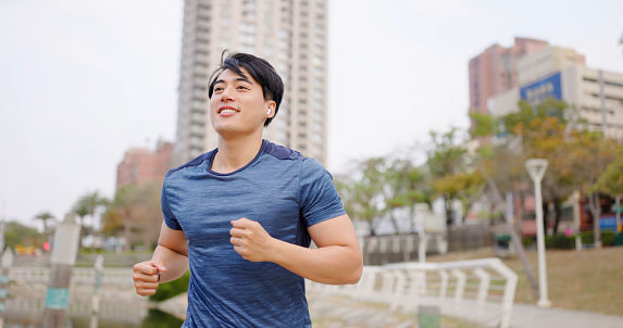 asian male runner wearing earbuds to listen music is jogging in city