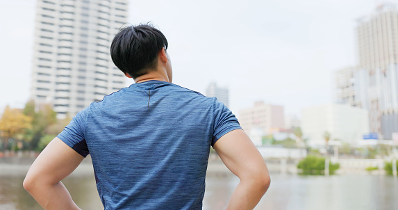 rear view asian male runner wearing earbuds to listen music is ready to jog outdoor - looking city view