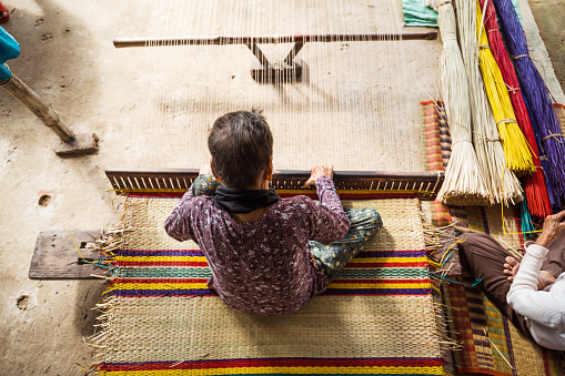 overhead view on vietnamese senior woman weaving bamboo mats, sitting on the floor