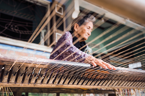 low angle view on vietnamese senior woman weaving bamboo mats, sitting on the floor