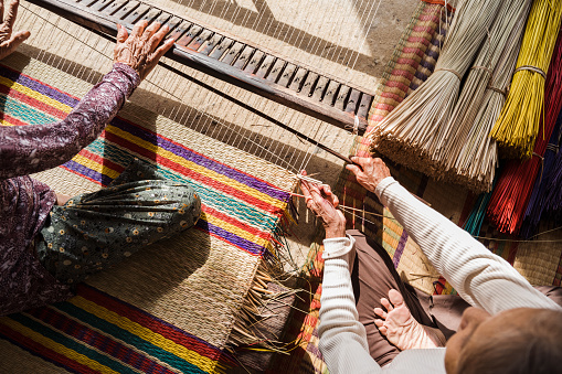 overhead view on vietnamese senior woman weaving bamboo mats, sitting on the floor