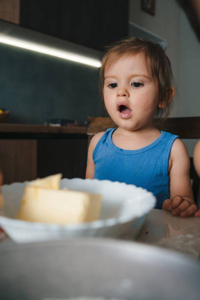 portrait en gros plan d’une petite fille debout, la bouche ouverte, choquée par la quantité de beurre que sa mère a mise dans l’assiette pour préparer des gâteaux faits maison. famille heureuse. préparation des aliments. nourriture sucrée. - family mouth open vertical mother photos et images de collection