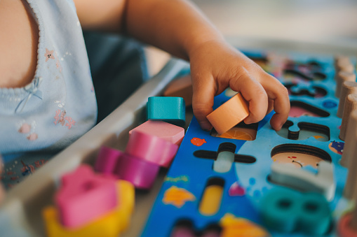 Close-up view of baby's hands playing in a puzzle made of colorful figurines. Education concept. Family activity concept. Happy family kid concept. Lifestyle concept. Family home leisure.