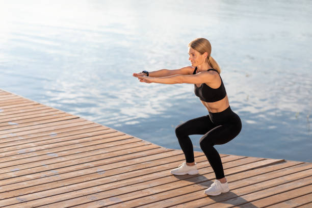 istock Outdoor Training. Smiling middle aged woman making squats exercise on the pier, 1474866940