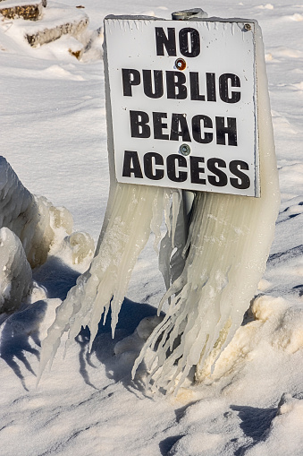 Beach sign covered in long icicles on extremely cold Winter day.
