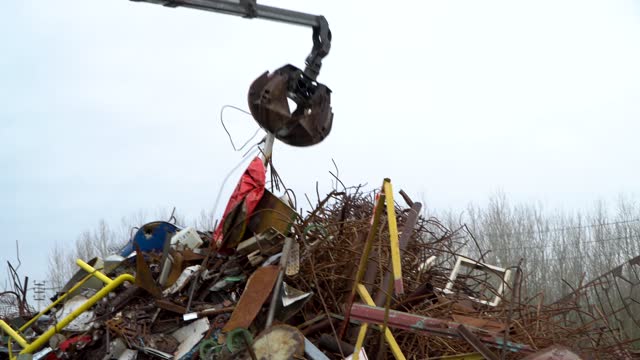 A grab loader loads industrial scrap metal for recycling. Manipulator with a hydraulic magnet crab on the background of the sky. The crane captures scrap metal.