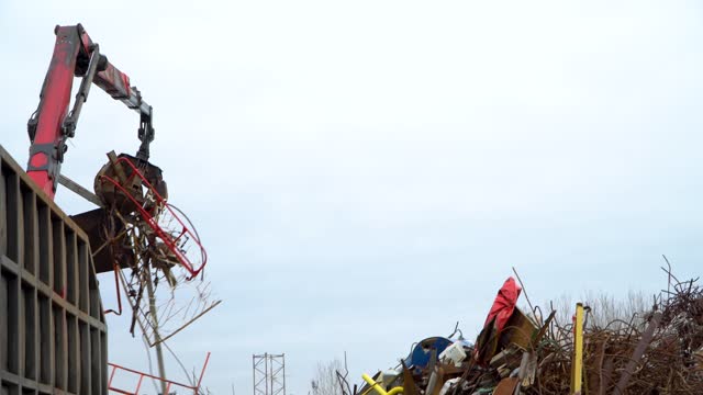 A grab loader loads industrial scrap metal for recycling. Manipulator with a hydraulic magnet crab on the background of the sky. The crane captures scrap metal.