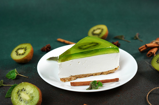 Cheesecake with Kiwi, cinnamon stick and leaves mint on a green background. Copy cpase for text