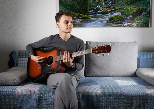 Young man playing an acoustic guitar on the sofa in the living room