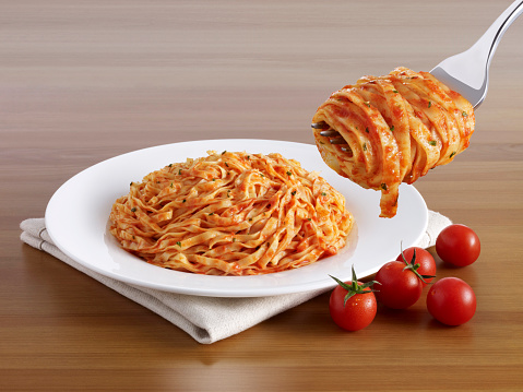 Forkful of delicious pasta in front of a pasta plate and dried chili pepper on a wooden table