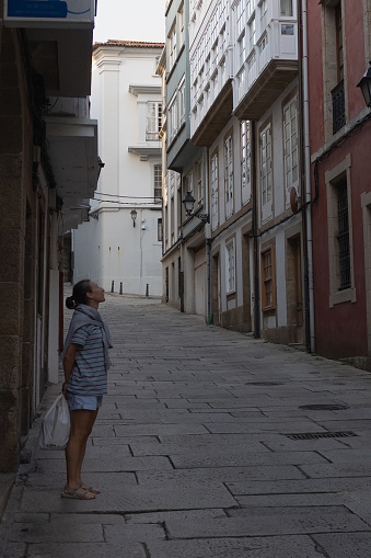 A full-length girl stands in the old city of Europe looking up at the building. The tourist considers the sights of the old town, narrow streets.
