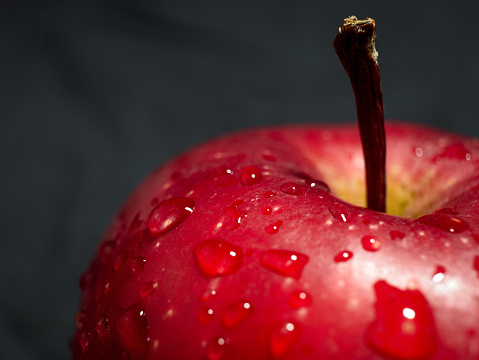 Close-up of delicious red apple and water drops on dark gray background