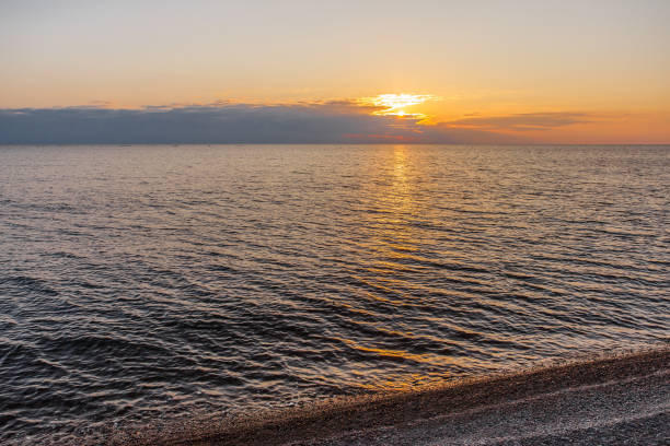 istock Sunset on sea red sun on horizon in clouds and pebble beach in foreground 1474876463