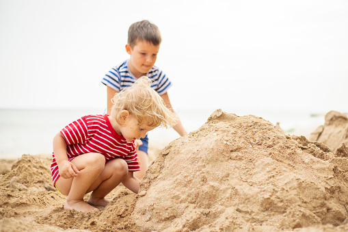 Two little boys are playing on sandy beach. Cute kids building sandcastles on beach in summer.