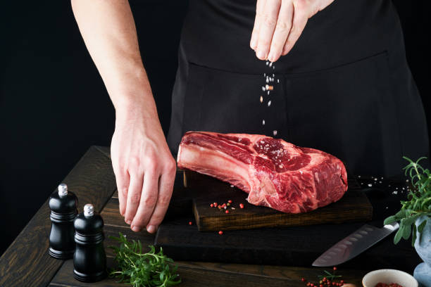 istock Chef cutting steak beef. Mans hands hold raw steak Tomahawk on rustic wooden cutting board on black background. Cooking, recipes and eating concept. Selective focus. 1474878818