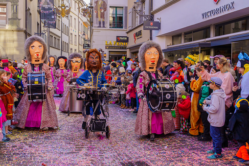 Lucerne, Switzerland - February 21, 2023: Group of participants in costumes march in the streets, and crowd, part of the children parade of the Fasnacht Carnival, in Lucerne (Luzern), Switzerland