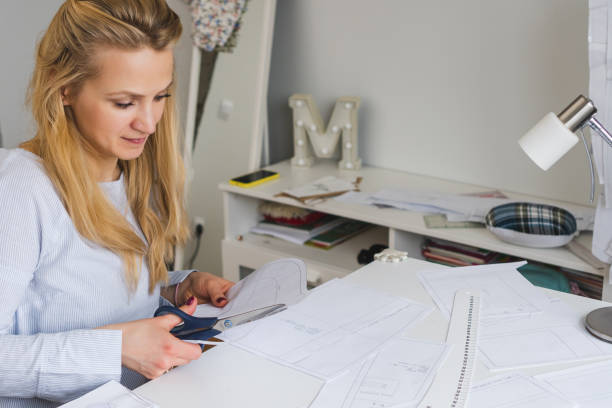 istock Seamstress cuts papper patterns for dress with scissors. Design development and clothes creating 1474881288