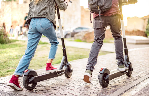 Millenial couple riding electric scooters at urban city park - Genz students using new ecological mean of transportation - Green eco energy concept with zero emission - Warm filter with sunshine halo stock photo