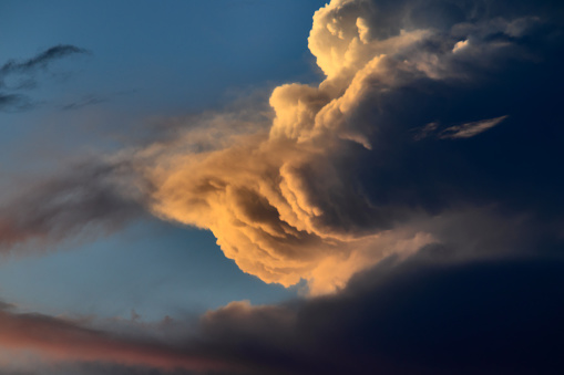 Large cumulus congestus cloud illuminated by twilight light, floating imposingly under a blue sky.