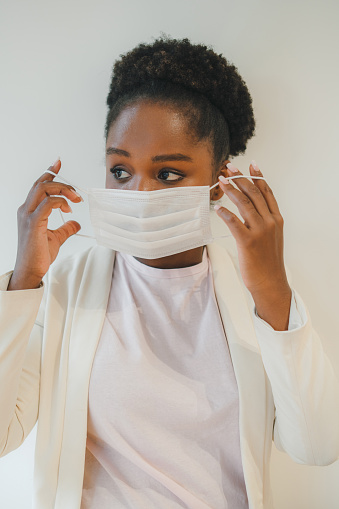 Studio portrait of young african woman putting on the protective medical mask, looking away with fear. Ioslated on white background.