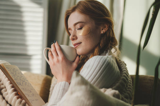 istock Attractive woman sitting on sofa in the morning, drinking tea, reading book, feeling comfortable at home, having rest. Home comfort. Cozy apartment. 1474885298