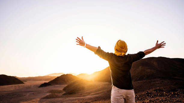 Happy man with arms outstretched standing on the top of the mountain enjoying sunset - Successful traveler with hands up celebrating victory outside - Travel, healthy lifestyle and winning concept stock photo