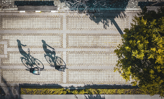 Aerial view of two cyclist and their shadows reflection on the road in public park at sunset