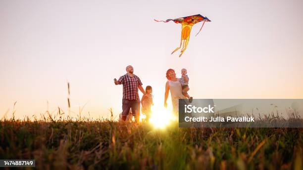 Panoramic Diversity View Of Family Running At Sunset With Kite In The Sky View From Below Stock Photo - Download Image Now