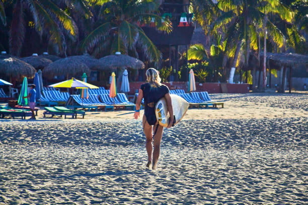 サーフボードとラウンジを背景に歩く女の子、ジカテラプエルトエスコンディードオアハカ - women sensuality surfing water sport ストックフォトと画像